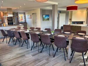 La salle à manger avec sa grande table et la cuisine ouverte